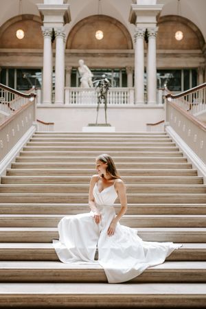A bride in a flowing white gown poses gracefully across grand marble steps of a neoclassical building.