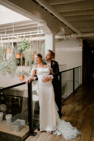 A couple embraces in an elegant indoor space with hanging plants and wooden floors during their wedding photoshoot.