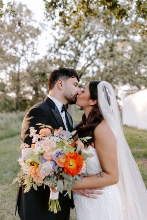 Romantic wedding couple shares intimate moments outdoors with colorful spring bouquet featuring orange and pink flowers.