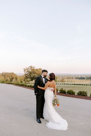 A romantic wedding couple shares a tender kiss on a scenic overlook during golden hour.