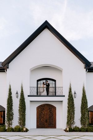 Modern white stucco building with arched wooden doors and tall cypress trees along the facade.
