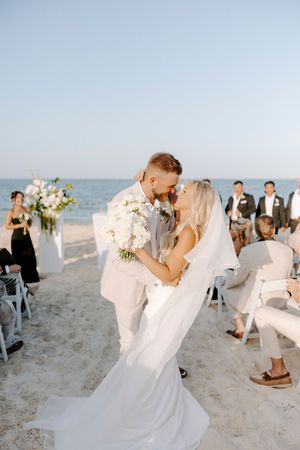 A romantic beach wedding ceremony with a couple sharing their first kiss as white chairs and ocean waves create a scenic backdrop.