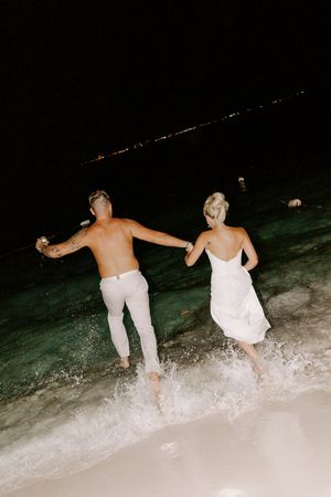 Carefree people running into ocean waves at night for a celebratory beach splash.