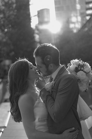 A romantic wedding couple shares a tender kiss at sunset with sunlight streaming through trees in the background.