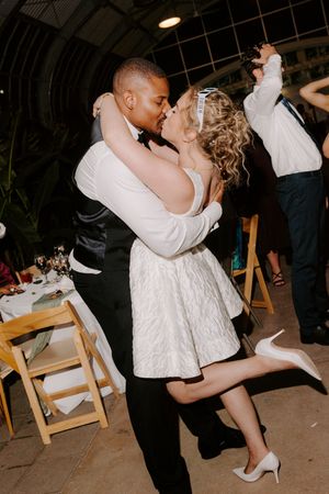 Bride and groom share a romantic kiss while dancing at their wedding reception, bride wearing short white dress.