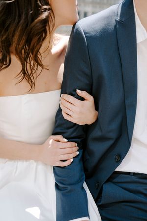 Close-up details of a couple embracing, showing a navy suit jacket and white dress in soft natural light.