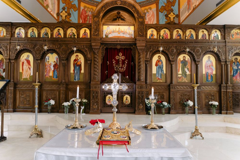 Interior view of an ornate Orthodox church with golden icons, white marble floors and decorative chandeliers.
