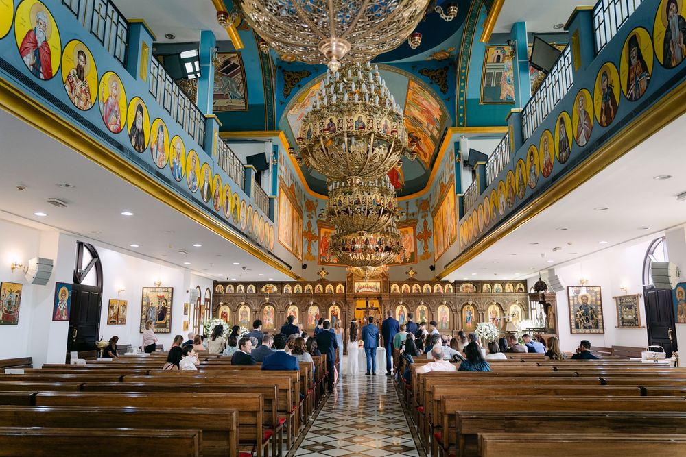 Interior view of a Catholic church with ornate blue ceiling murals, crystal chandeliers, and wooden pews.