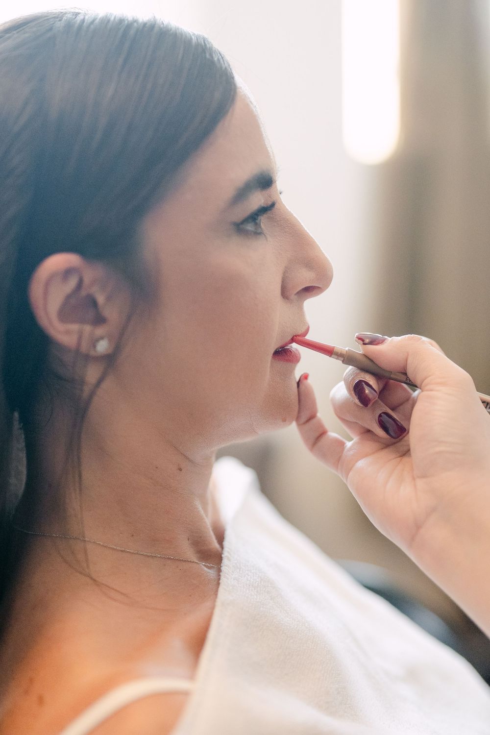 Close-up profile view of someone getting lipstick applied by a makeup artist's hand wearing dark nail polish.