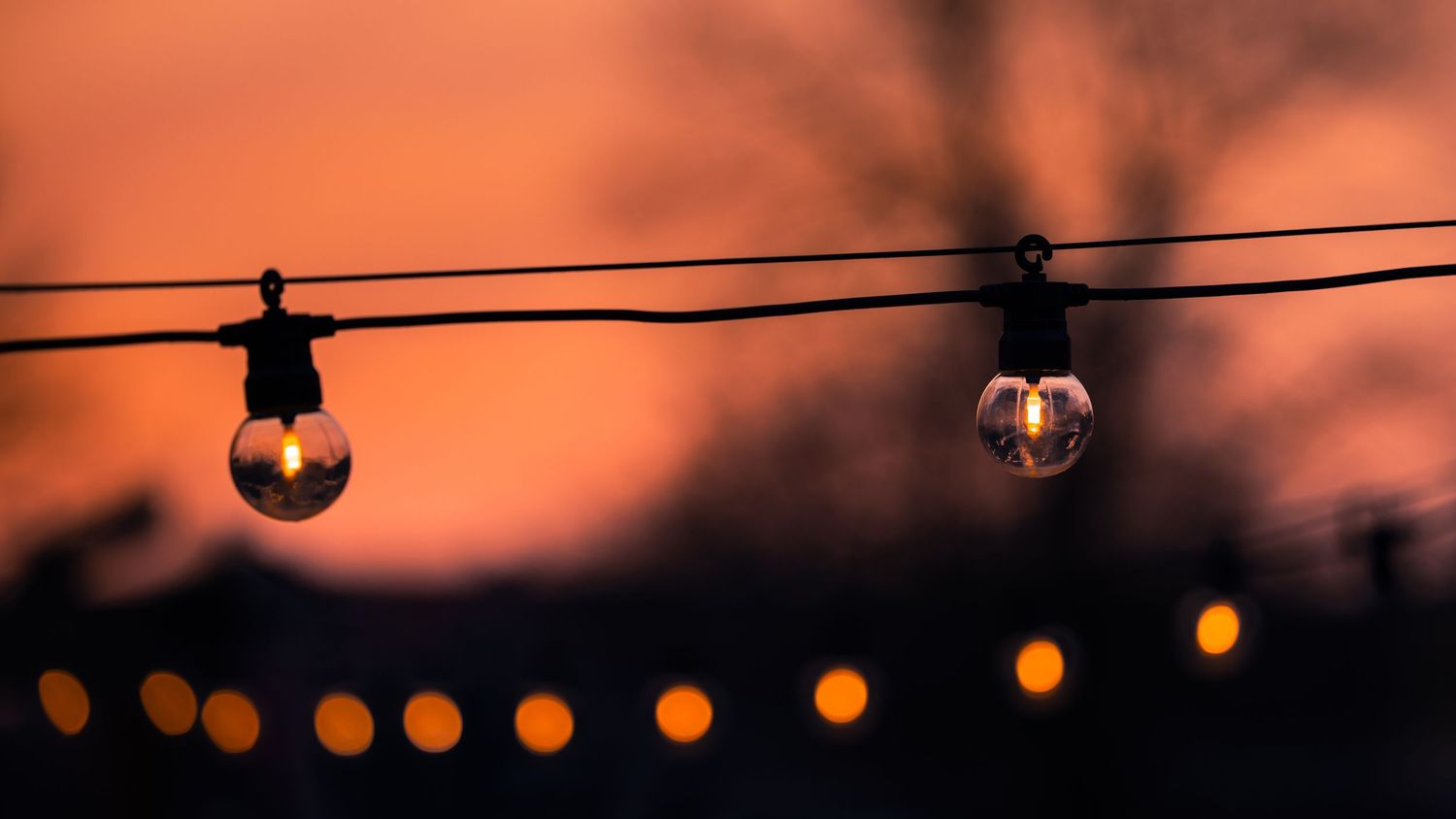 String lights glow warmly against a dusky orange sky creating a magical outdoor ambiance at sunset.