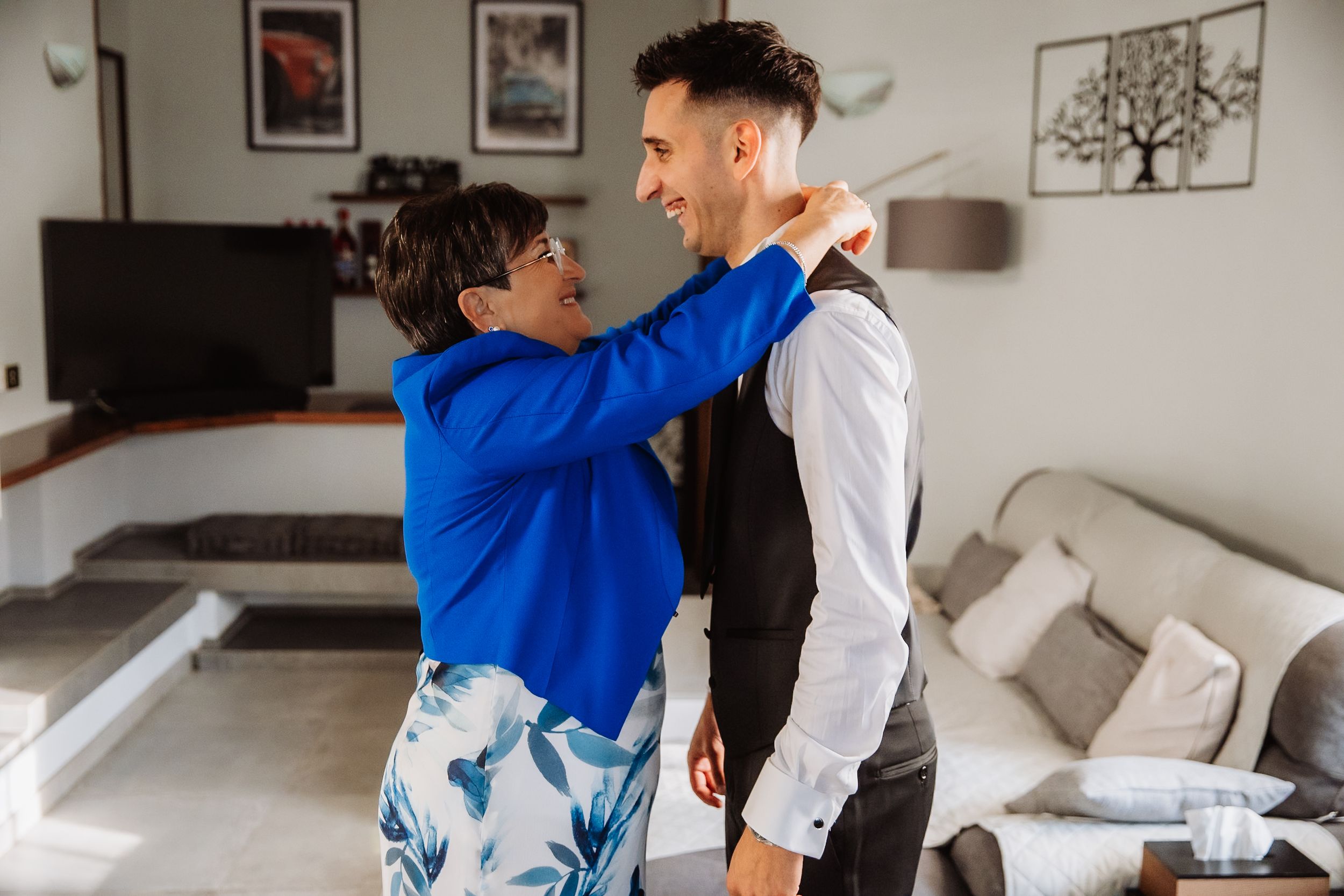 A couple in blue and white outfits dance together in a bright room with framed artwork on the walls.