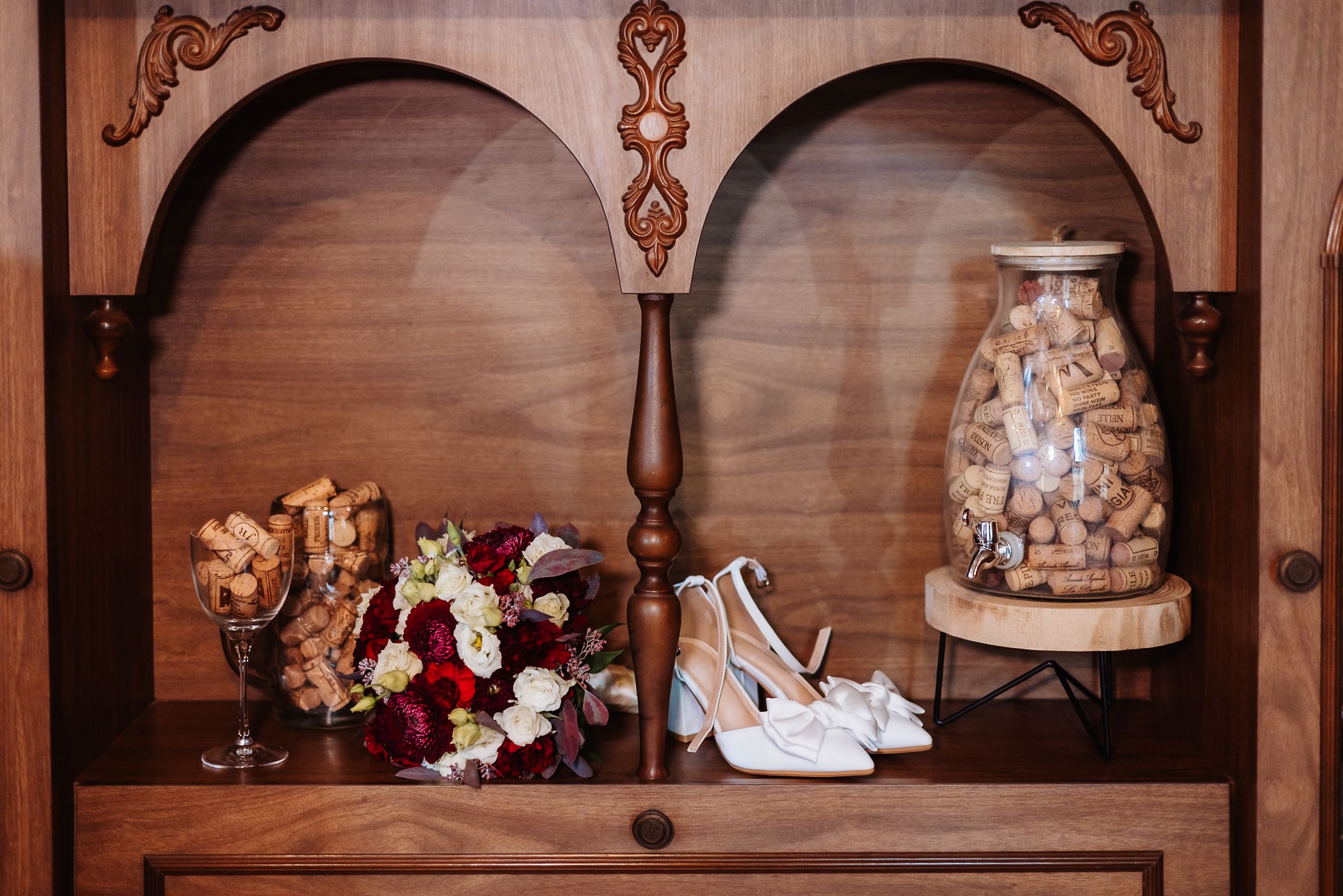 A rustic wooden shelf displays vintage glass bottles, white ceramic vases, and delicate floral arrangements in warm lighting.