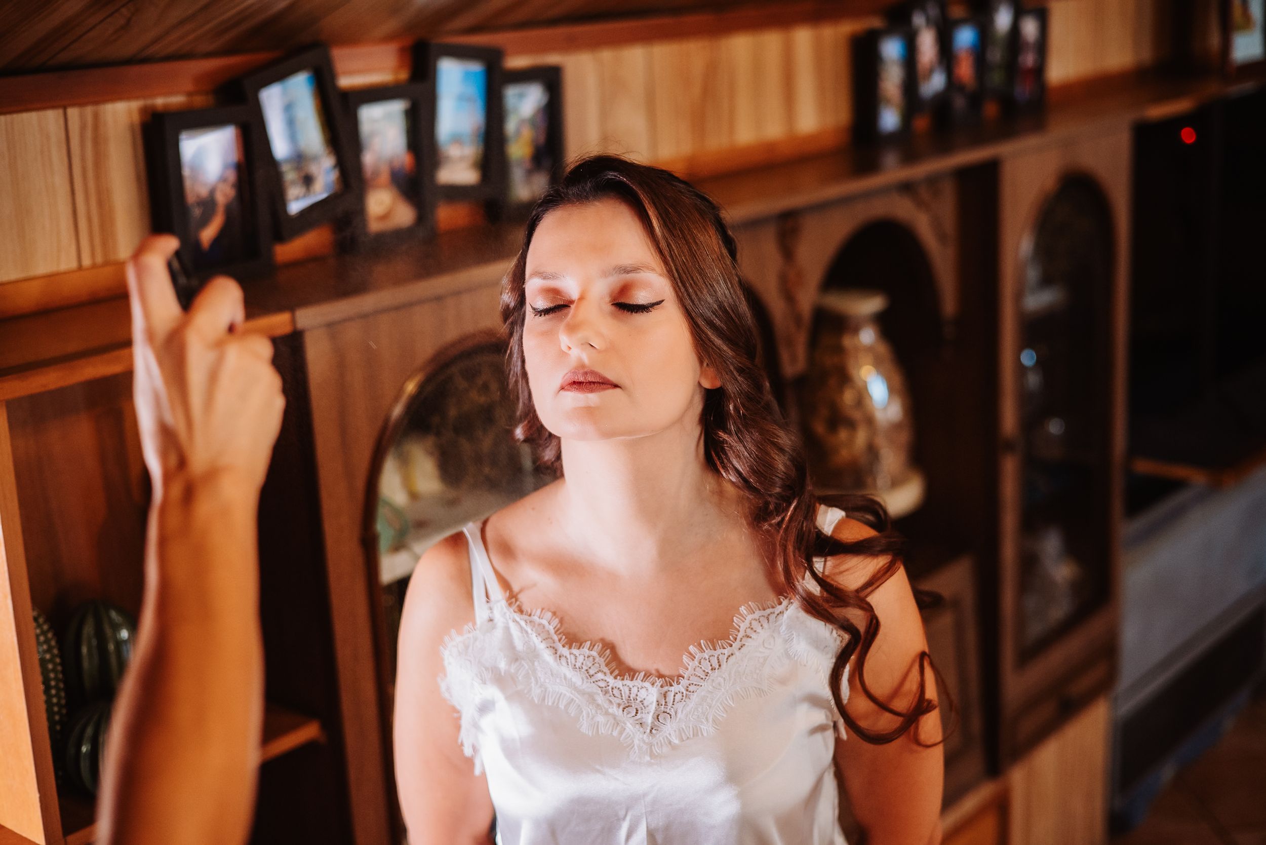 A bride in a white lace dress poses gracefully in a warm-lit rustic indoor setting.