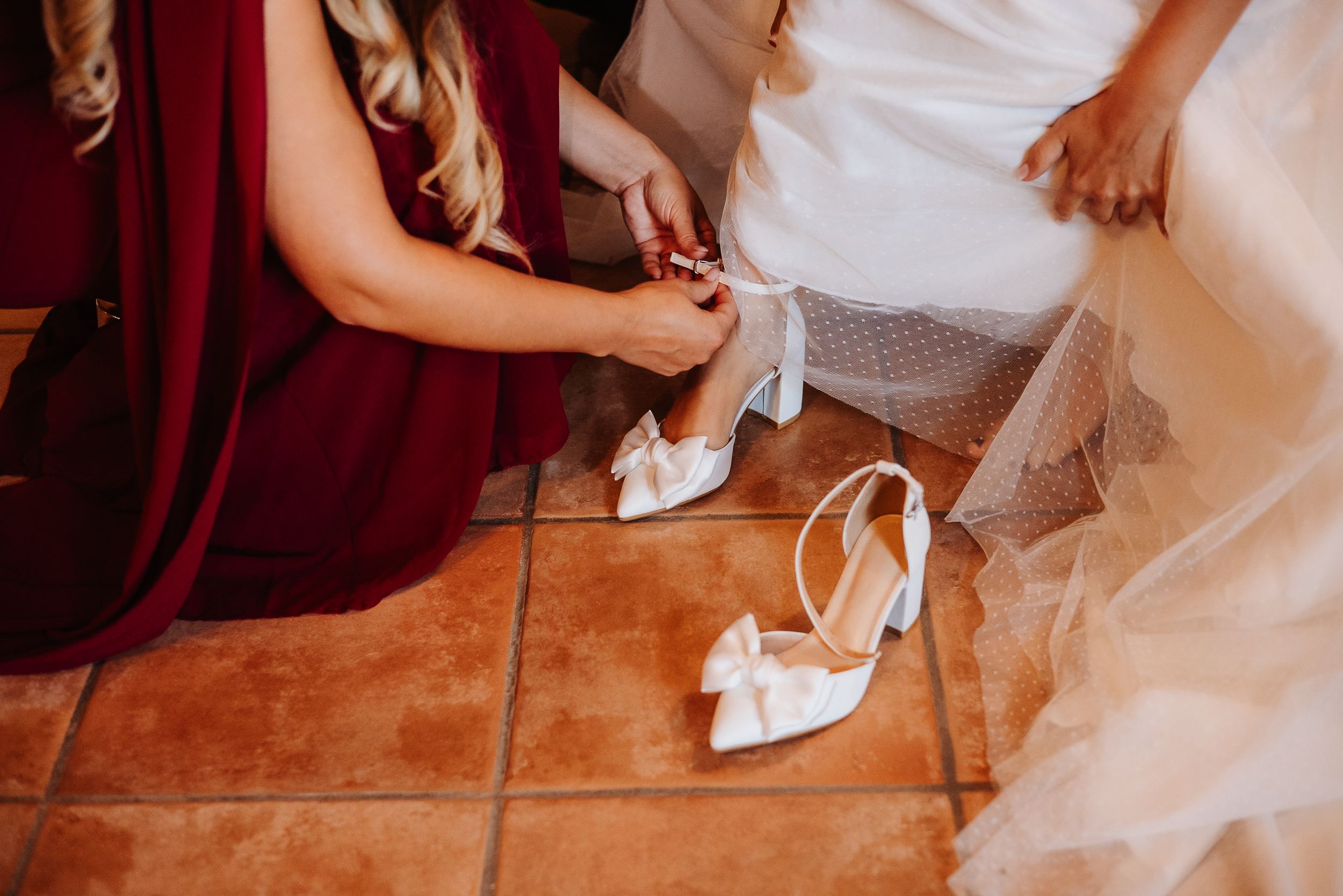 A row of wedding guests' feet and shoes arranged in a line on a terracotta tile floor.