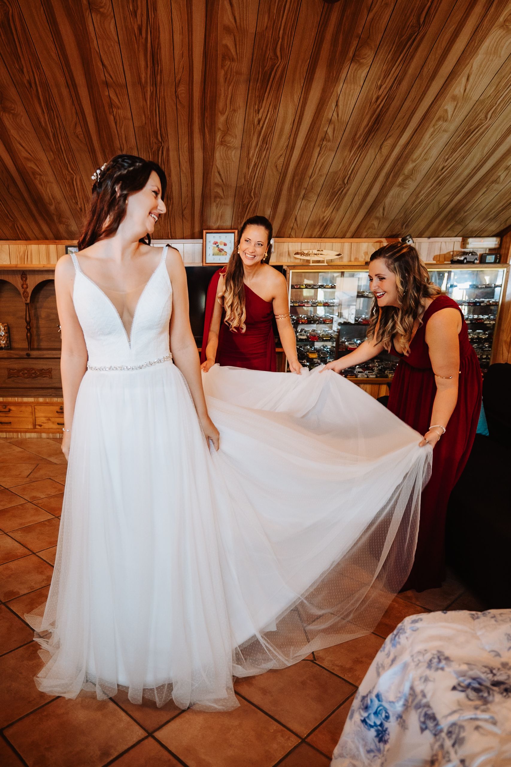 A white wedding dress being fluffed and styled in a rustic wooden room with warm lighting.