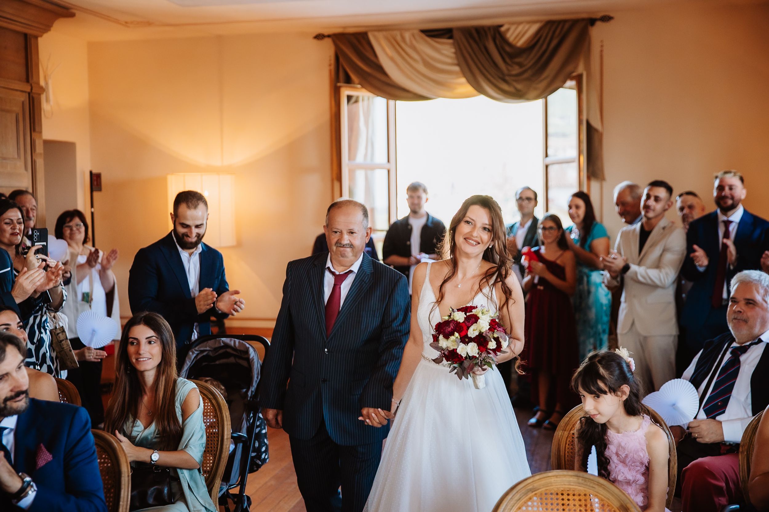 Wedding guests mingle and socialize in an elegant reception hall with warm lighting and cream-colored walls.