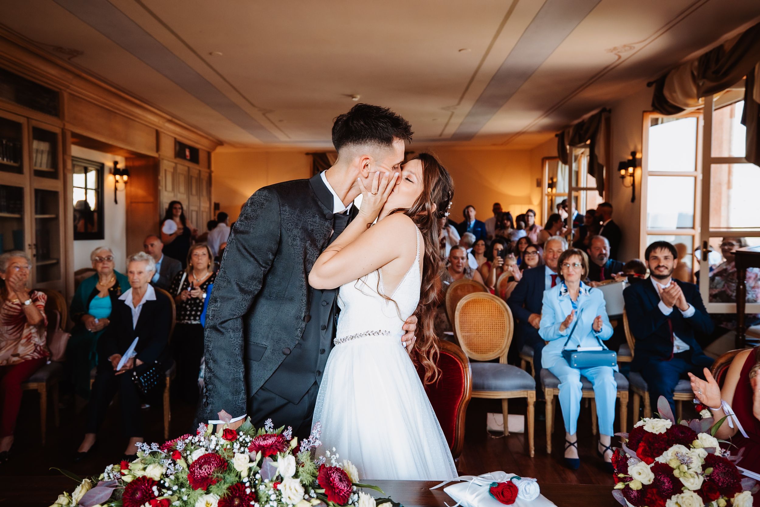 Wedding guests celebrate and dance during a joyful reception in a warmly lit venue with floral decorations.