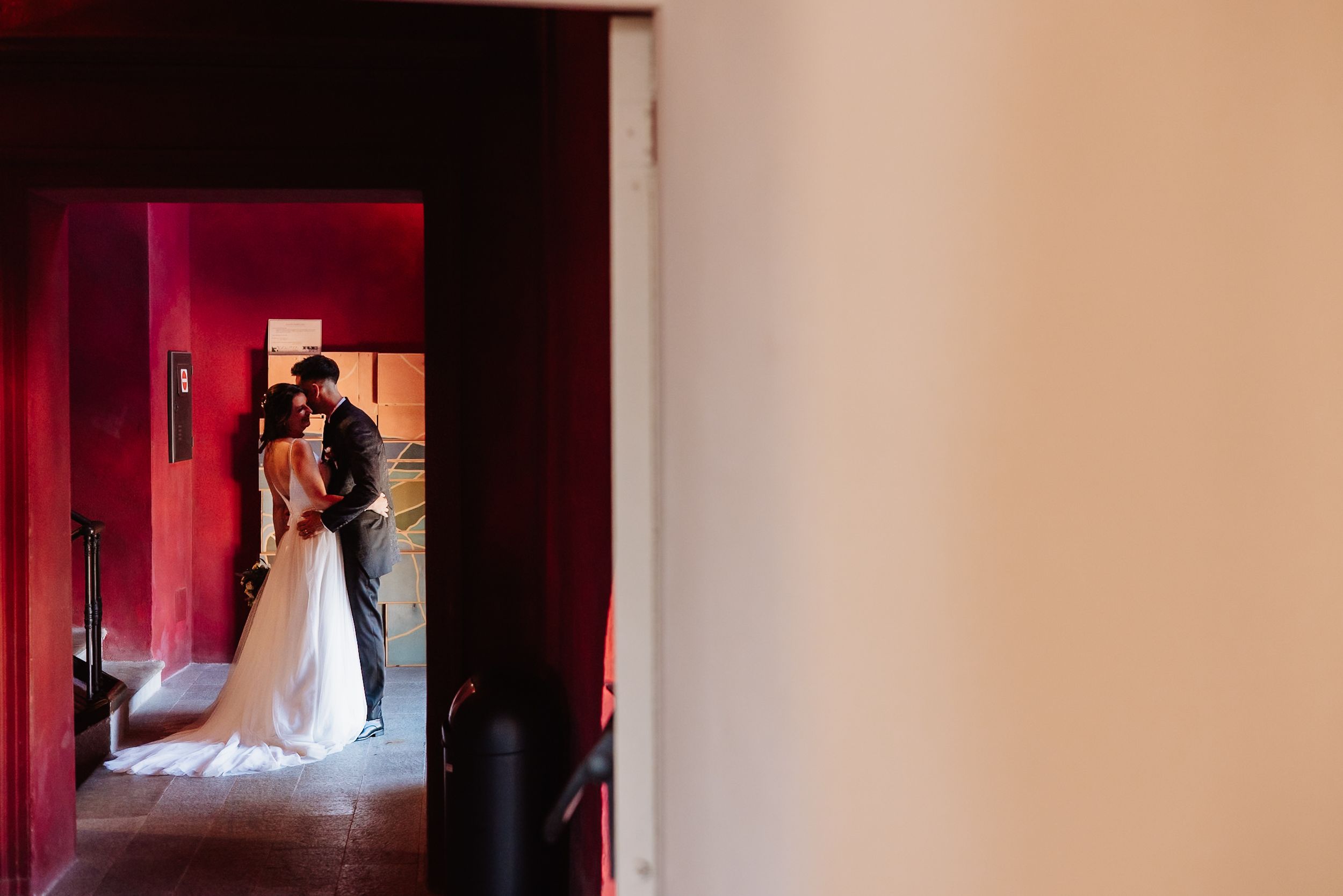 A wedding couple walks through a red-lit hallway in a dramatic sequence of six connected photos.