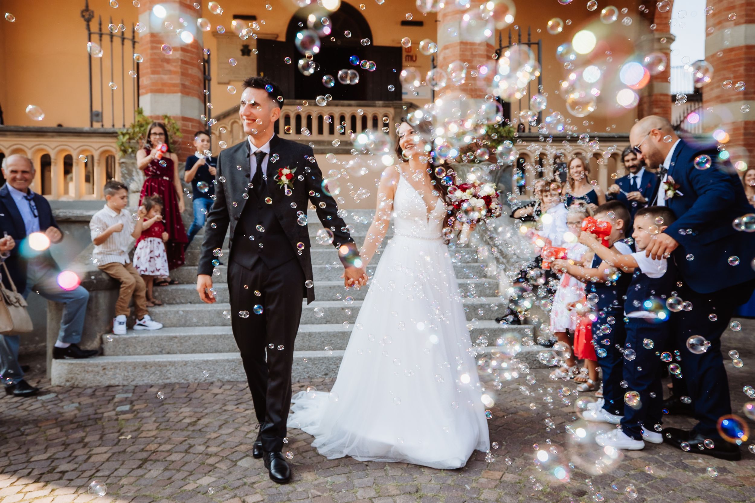 Wedding guests throw confetti and flower petals at a couple exiting a church ceremony in a joyous celebration.