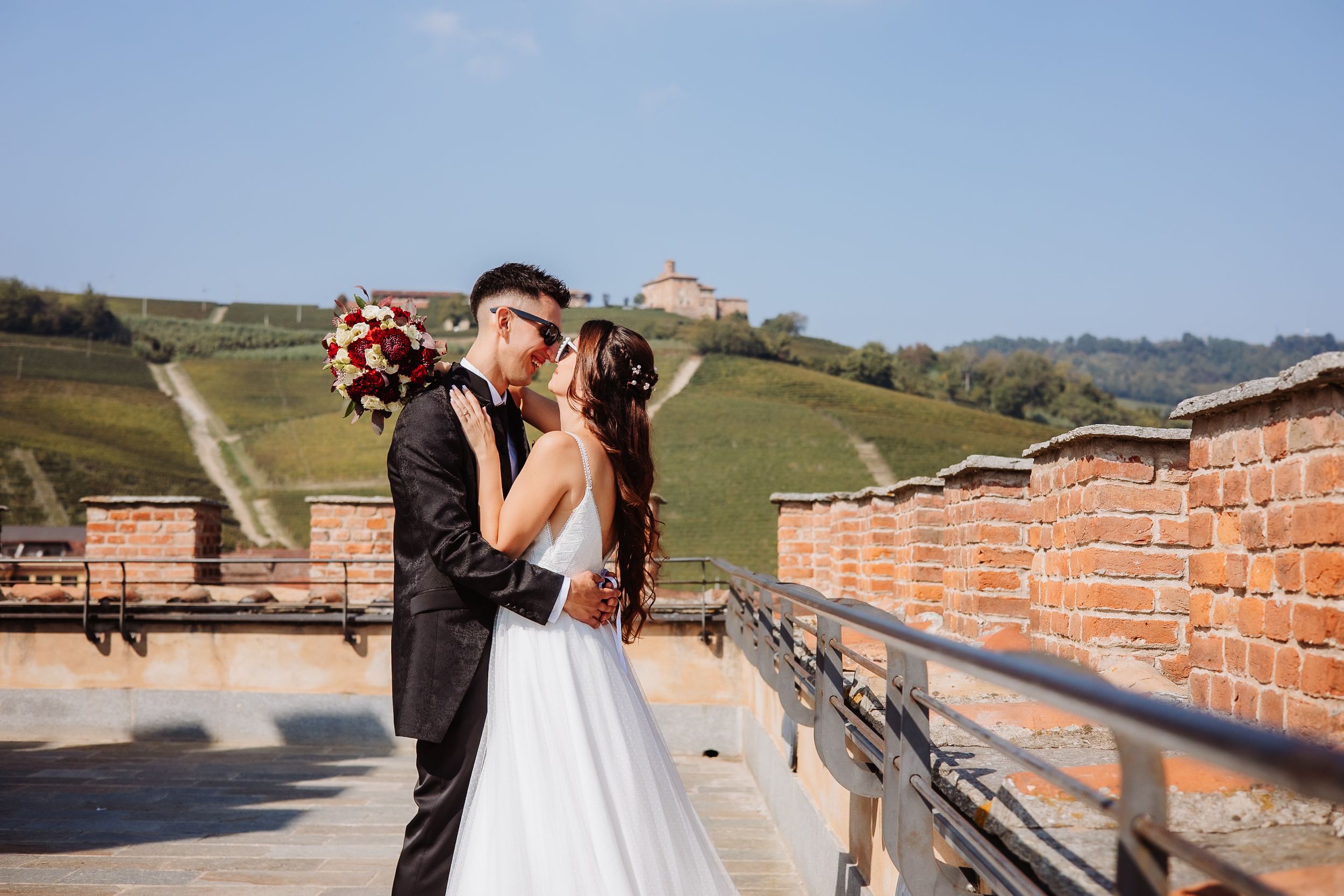 Wedding couple poses together along a scenic countryside path with brick walls and rolling hills in background.