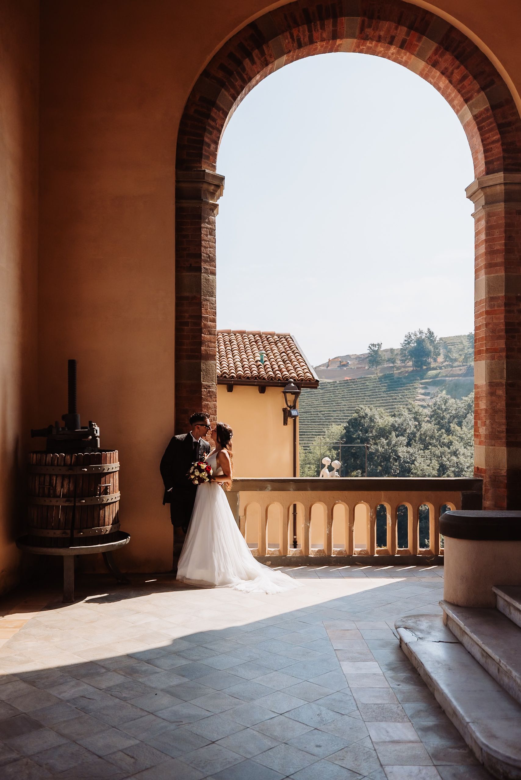 A romantic wedding couple shares an intimate moment under stone archways overlooking a scenic mountain landscape.