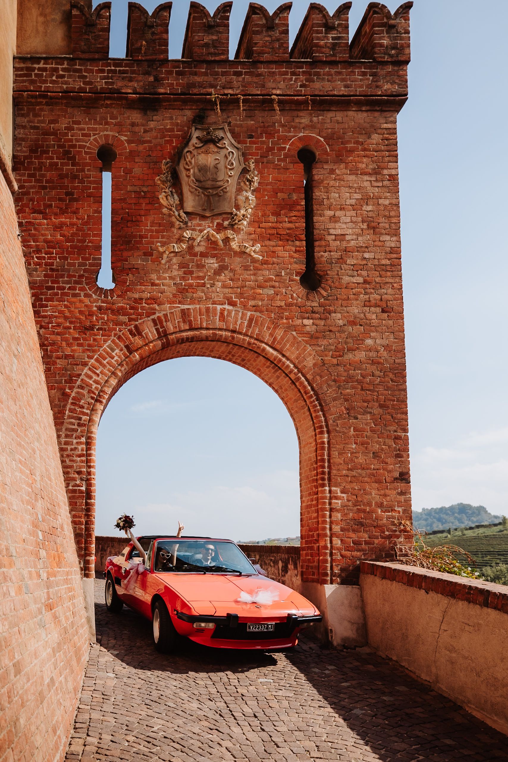 A red Ferrari sports car parked under a series of brick archways at a historic building location.