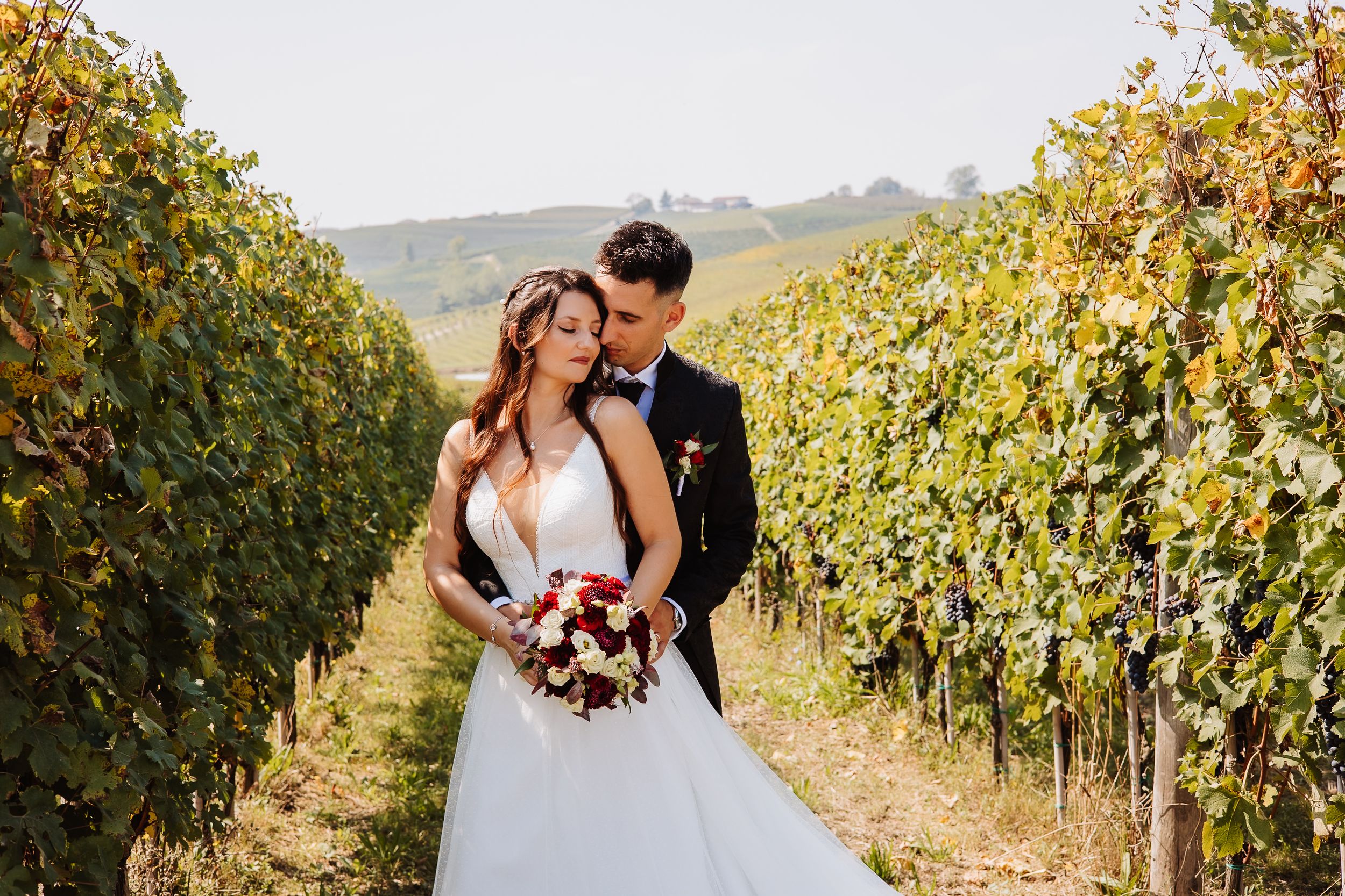 Romantic couple embraces in a sun-drenched vineyard during autumn harvest season.