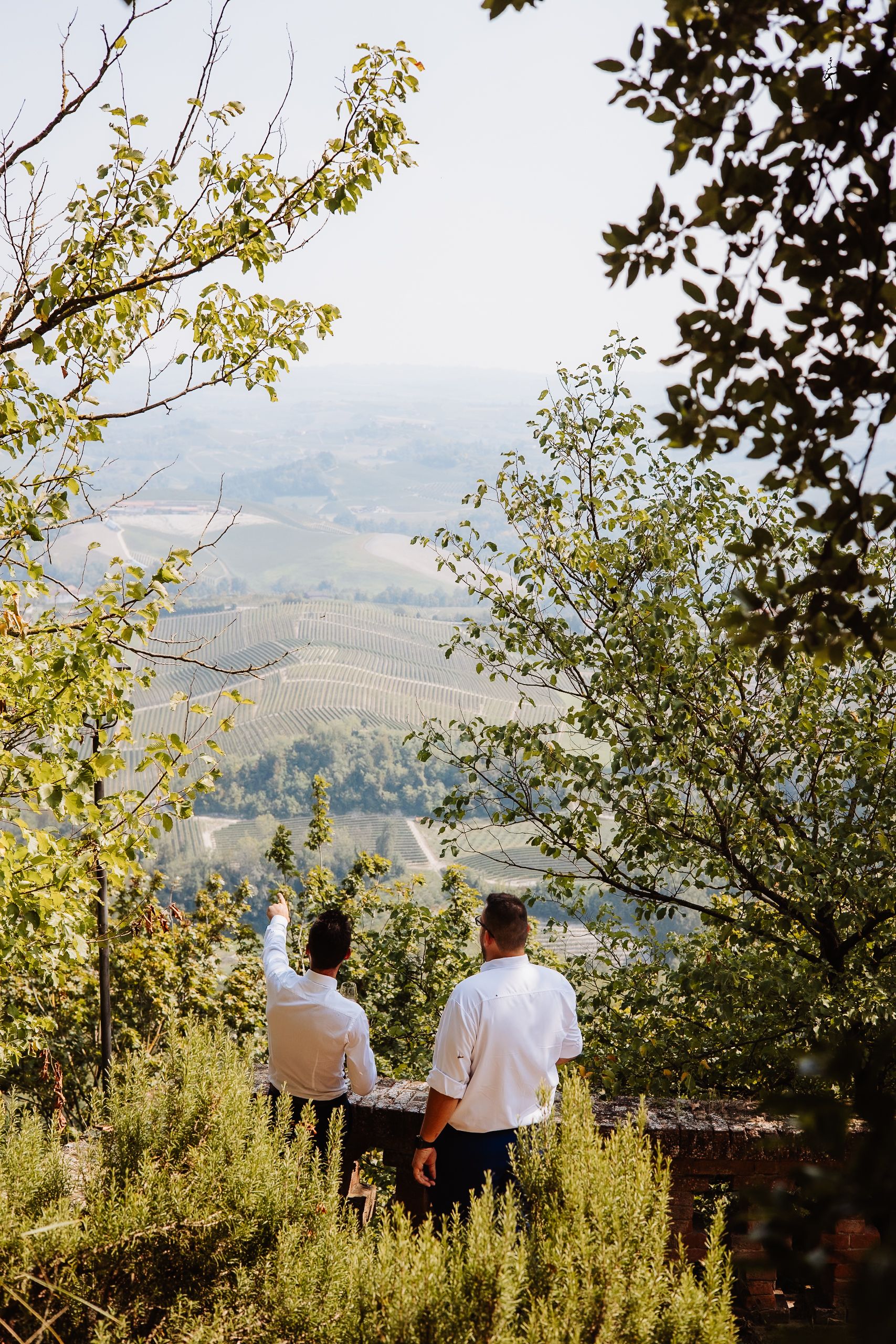 Two people stand on a scenic overlook enjoying views of rolling hills and a winding road through the countryside.