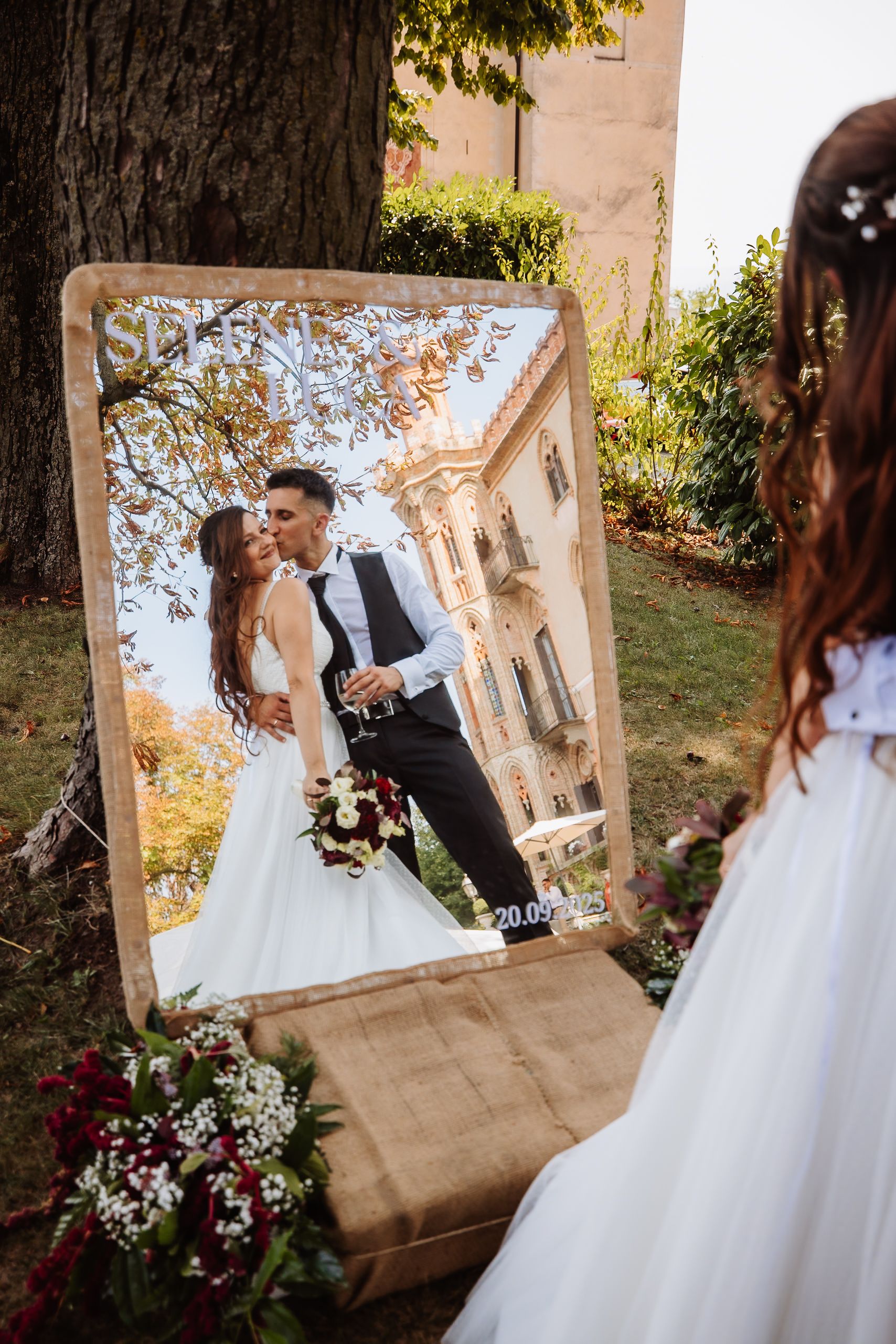 A creative wedding photo composition showing a couple's reflection in an elegant mirror set up outdoors with autumn foliage.