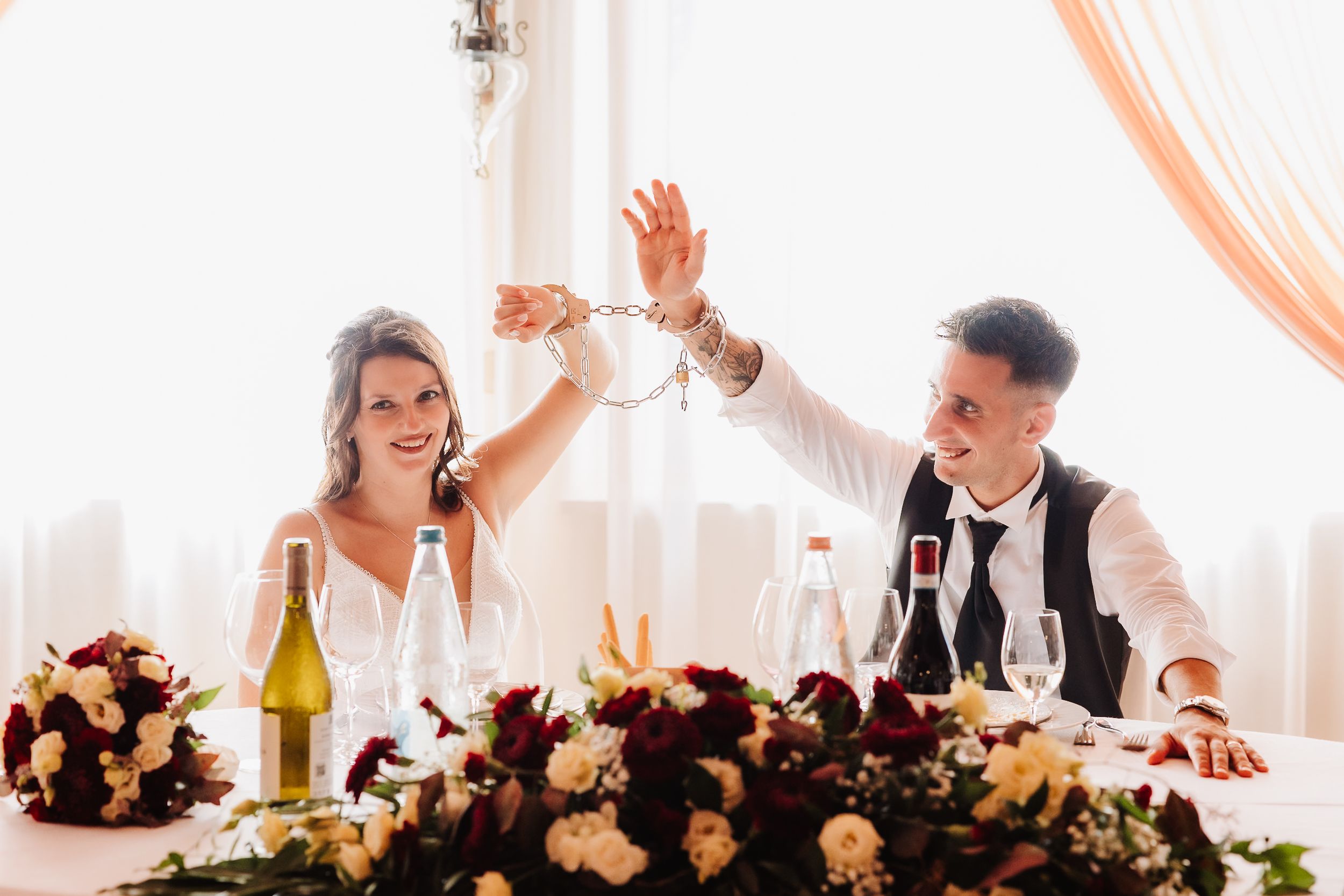Guests seated at a long table during an elegant wedding reception with soft peach drapery and floral centerpieces.
