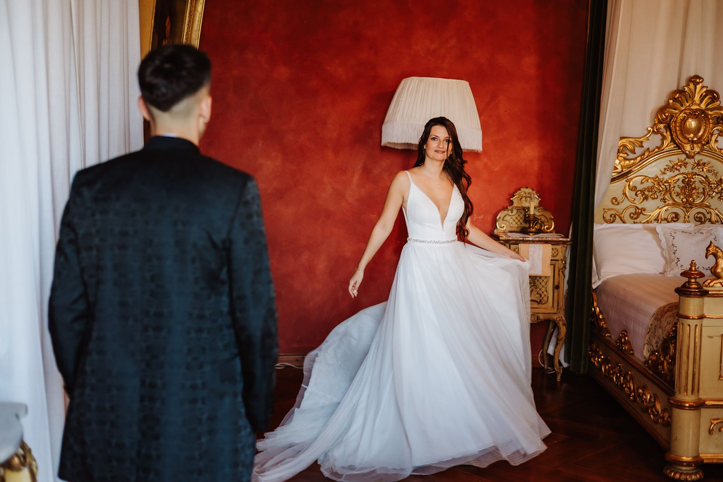 A bride in a white wedding dress twirls gracefully in a luxurious room with deep red walls and ornate gold decor.