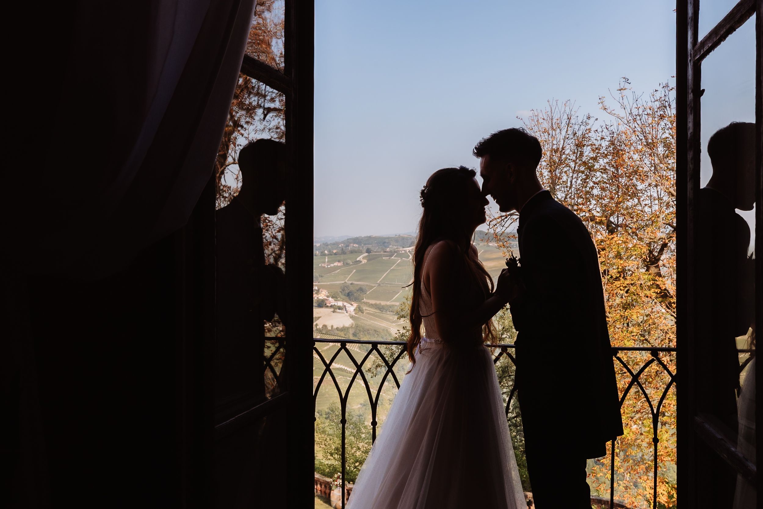 Silhouetted couple embraces by window with autumn foliage and mountain landscape in background.