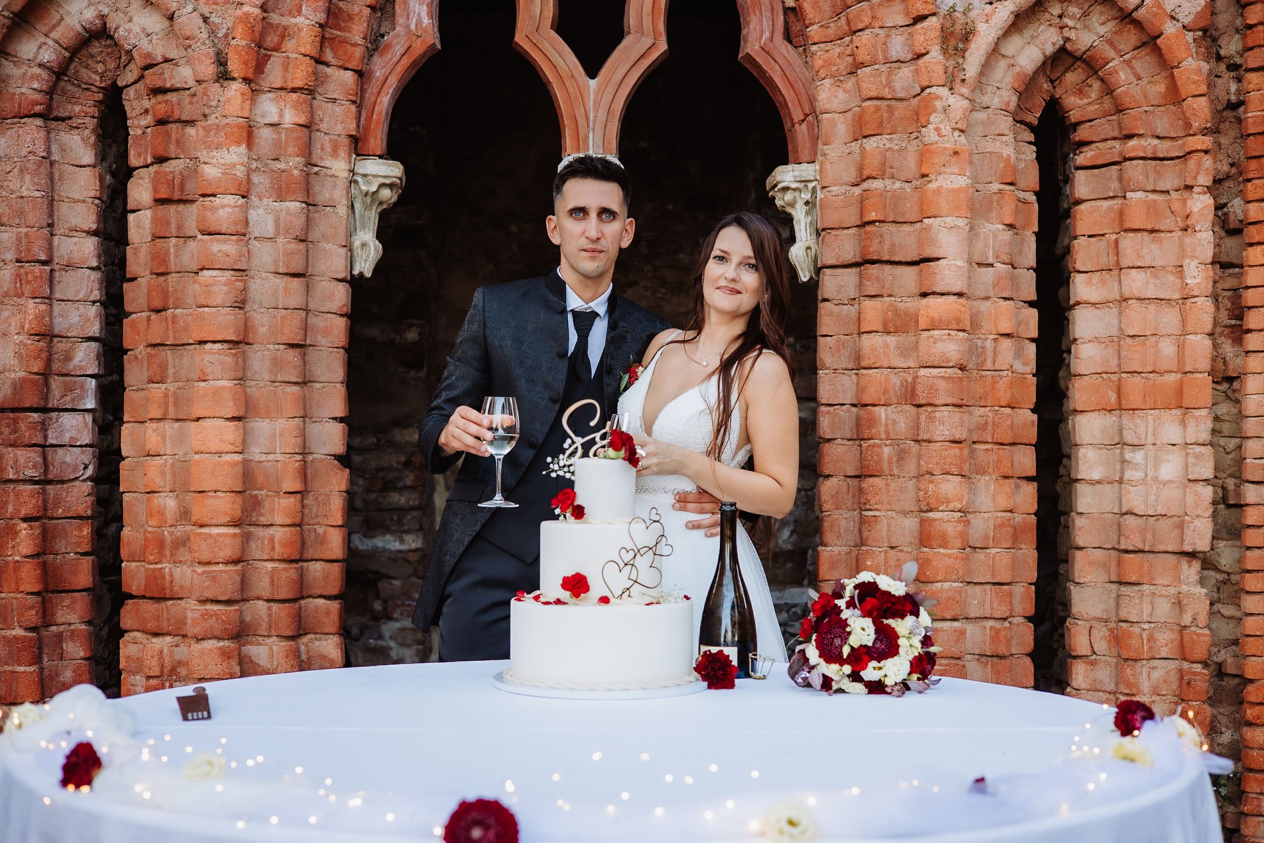 A wedding party celebrates at a rustic brick venue decorated with red roses and white linens.