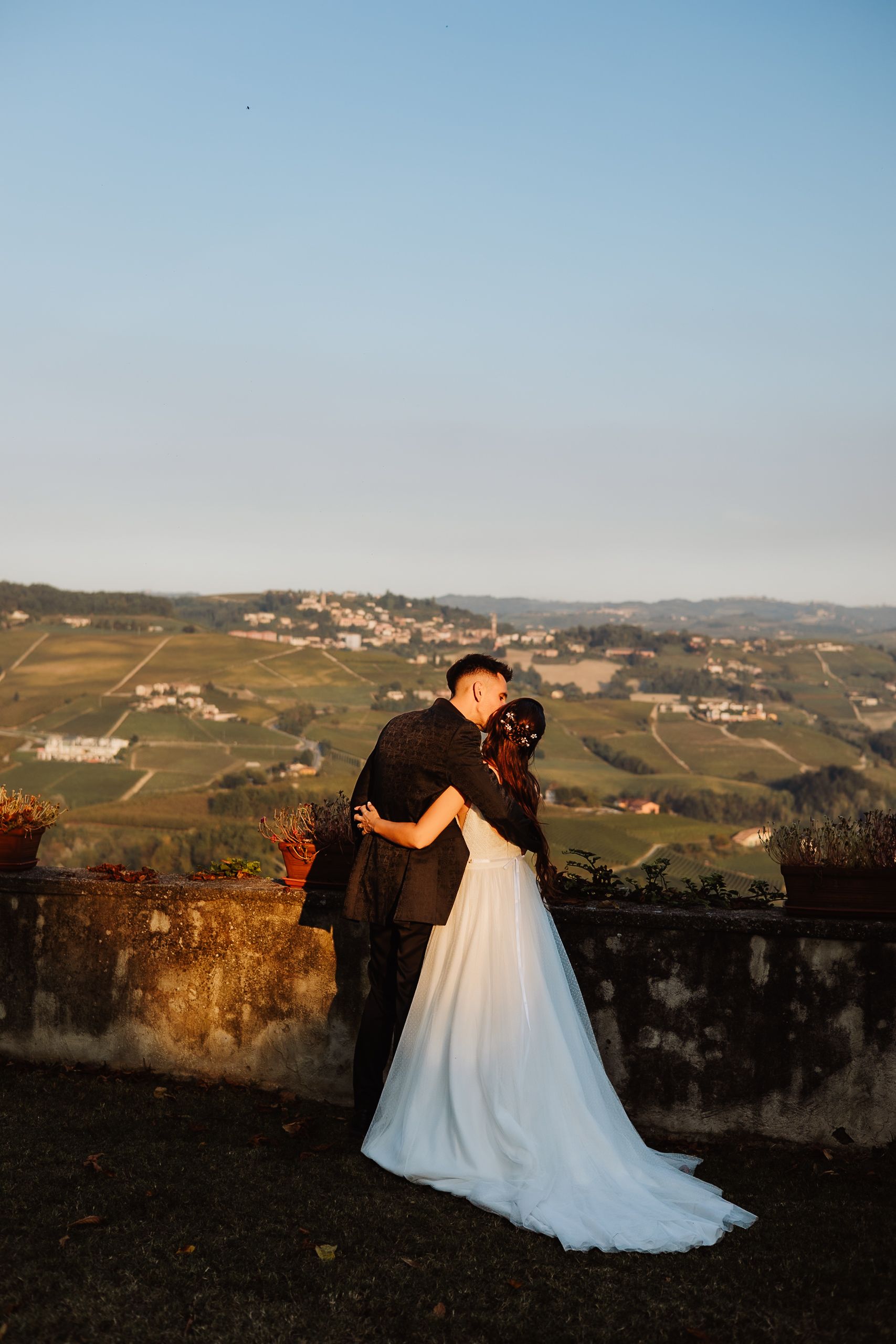 Romantic couple embraces at sunset overlooking scenic Italian vineyard hills in the Piedmont region.