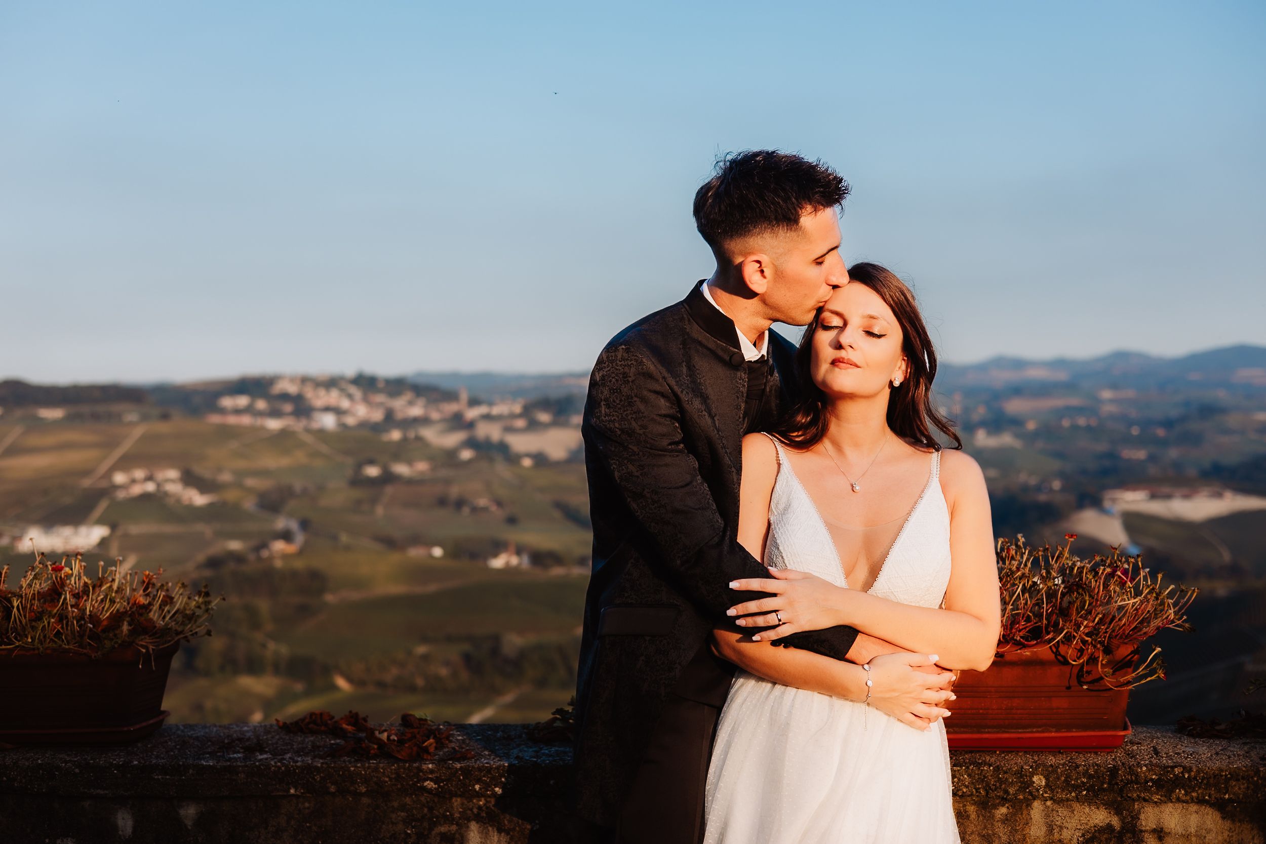 A couple shares a romantic moment at sunset overlooking rolling hills and vineyards in the countryside.