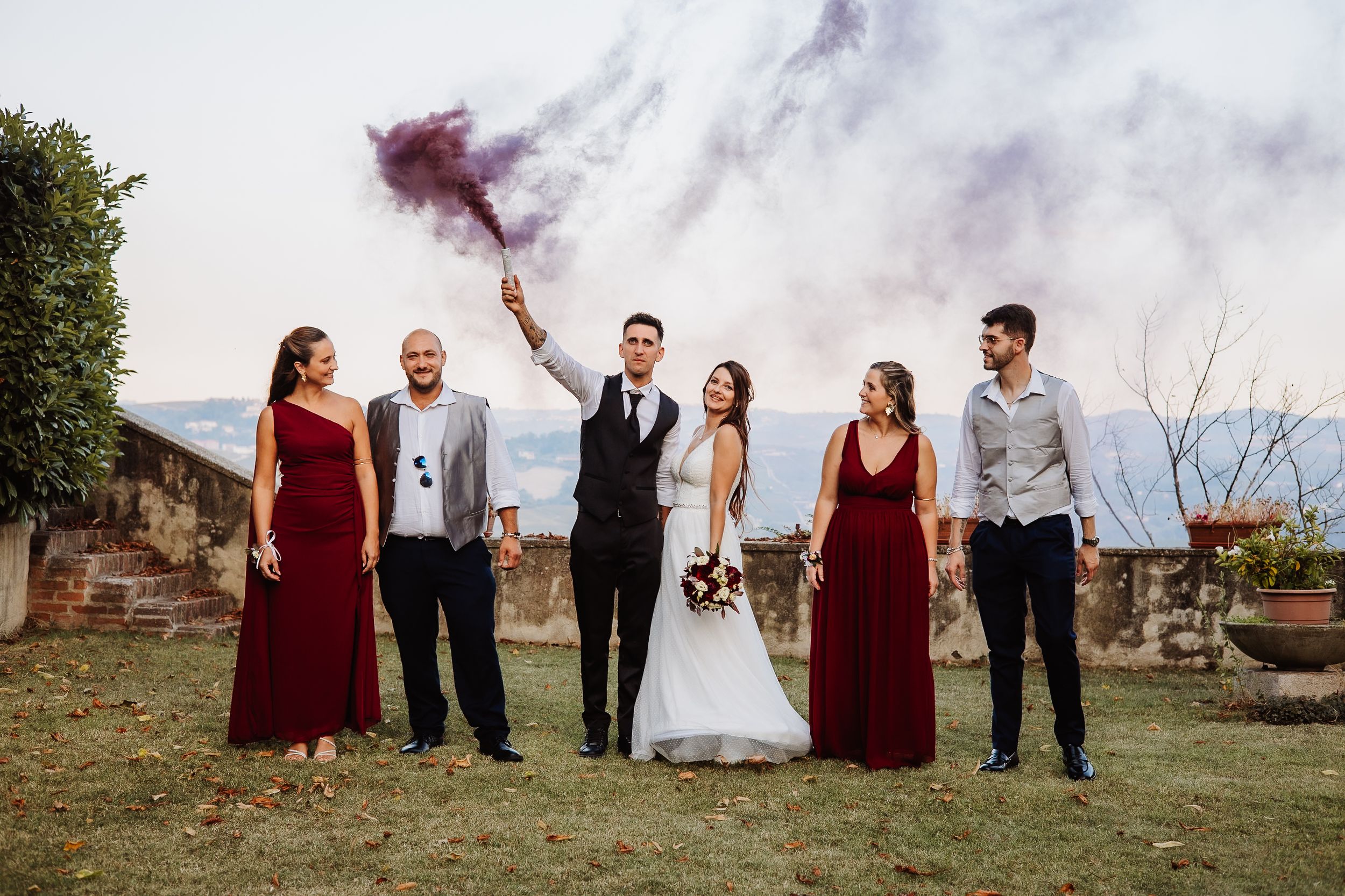 Wedding party in burgundy and neutral attire poses together in a scenic outdoor setting during golden hour.