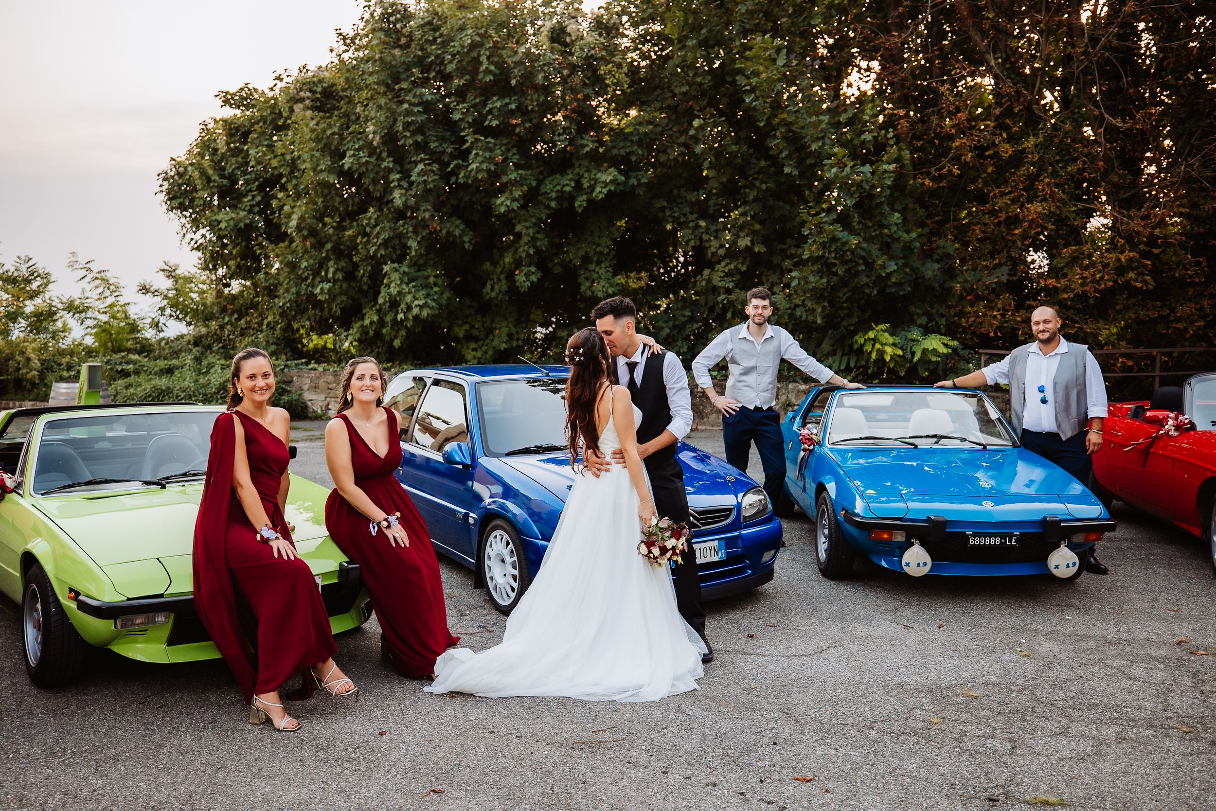 A series of wedding photos showing people posing with classic vintage cars at an outdoor venue.