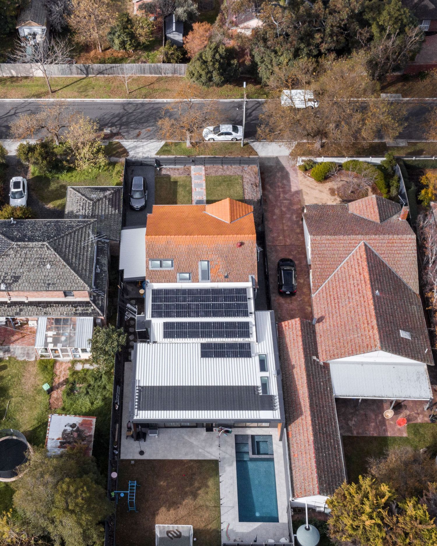 Bird's eye view of residential house with solar panels and pool in suburban setting.