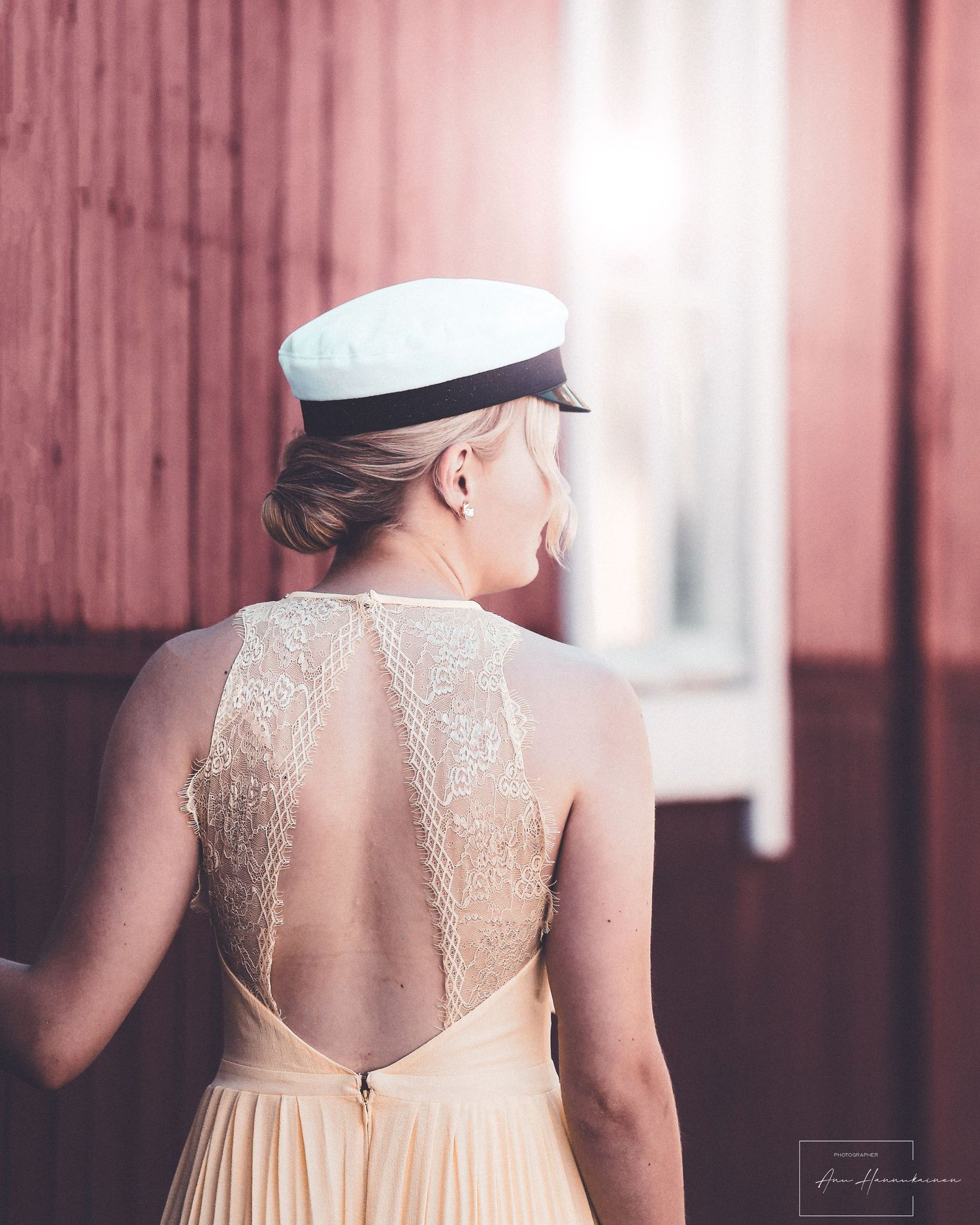 A bride in an elegant cream-colored dress with intricate lace back detail and vintage sailor cap looks away pensively.
