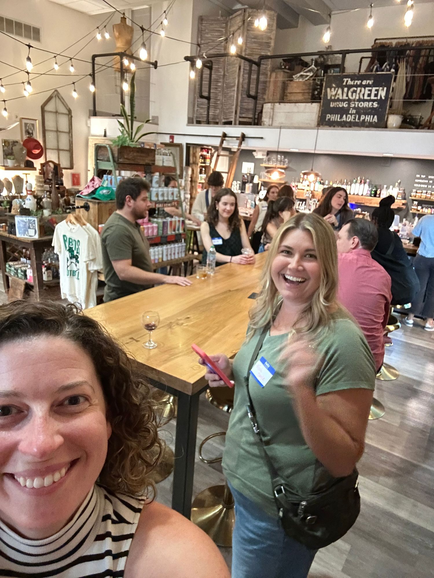 Friends enjoying drinks at a rustic retail space with string lights and decorative elements in a cozy modern setting.