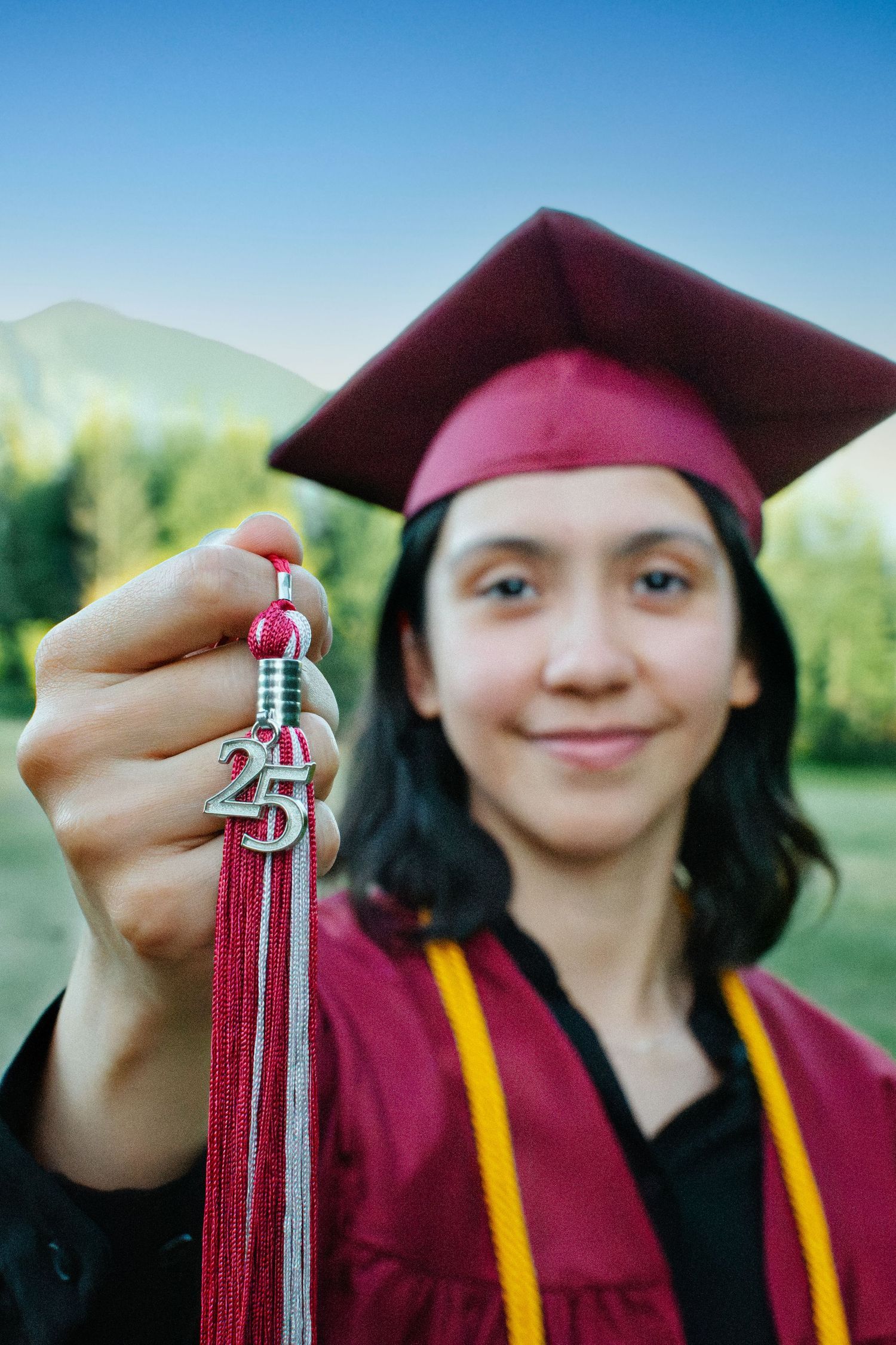 Graduate holding 2025 tassel with trees and mountains in background. Seattle graduation photography.
