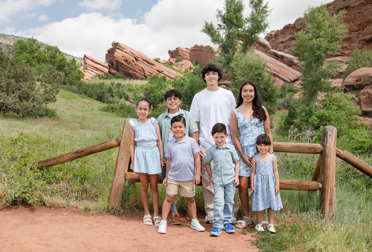 A family group poses together in front of the iconic red rocks at Colorado's scenic Red Rocks Park on a sunny day.