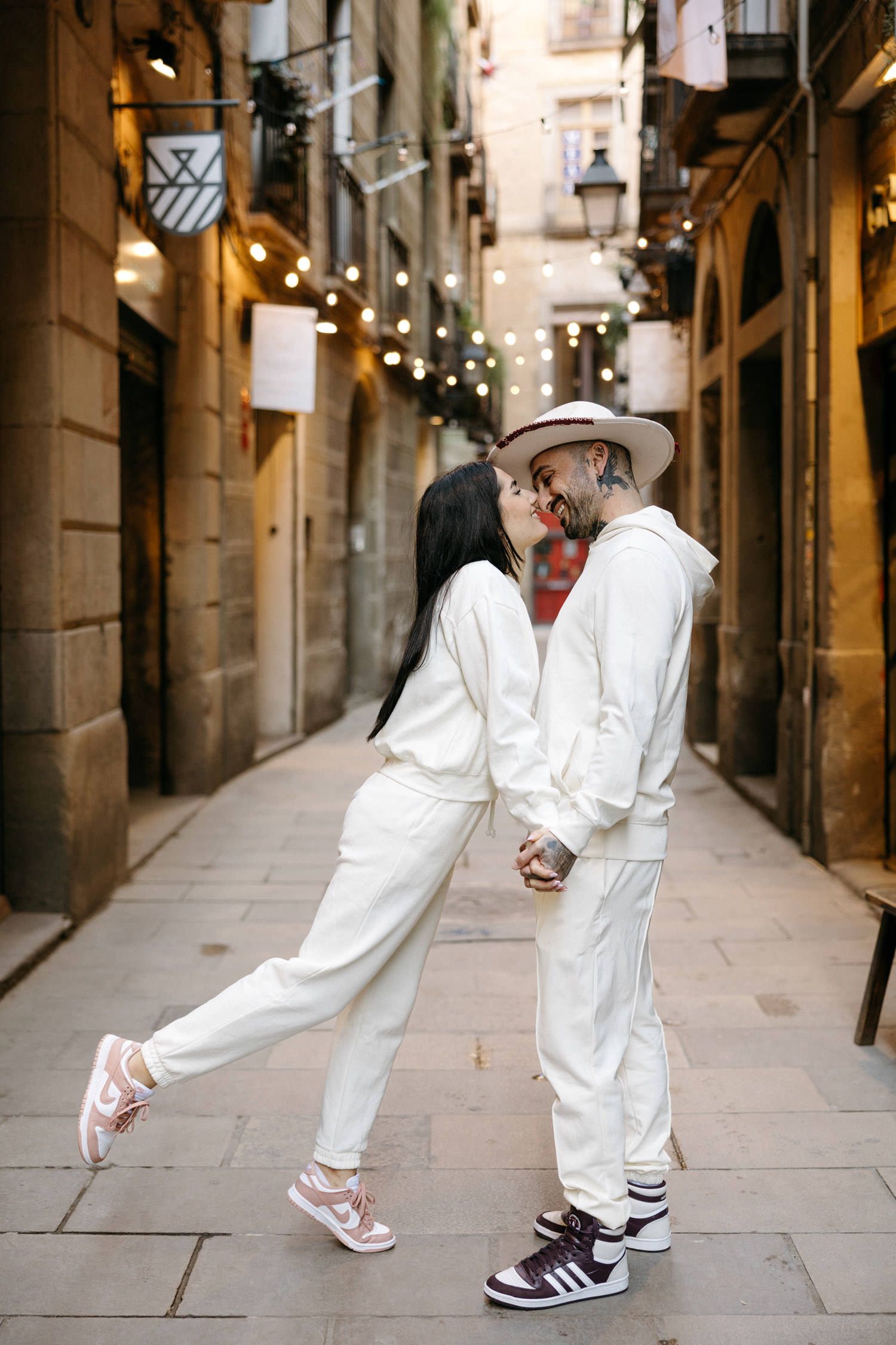 Playful couple in white outfits dancing in a charming European alleyway.
