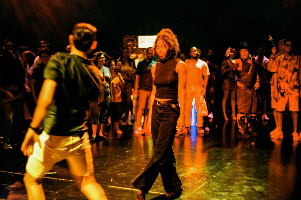 Dancers move together on a dimly lit dance floor with vibrant lighting effects during a social dance event.