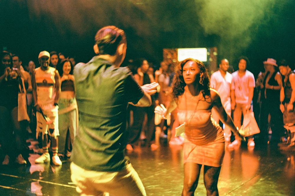 People dancing together in a large dimly lit room with warm atmospheric lighting and dynamic movement.
