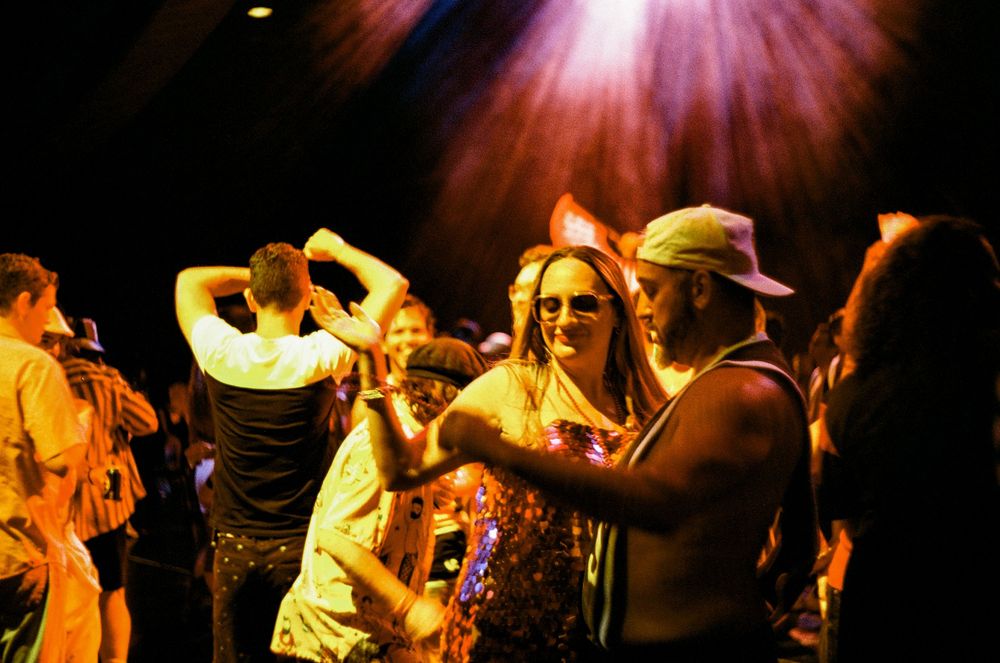 Clubgoers dance beneath pink lighting at a nightclub with energetic atmosphere.