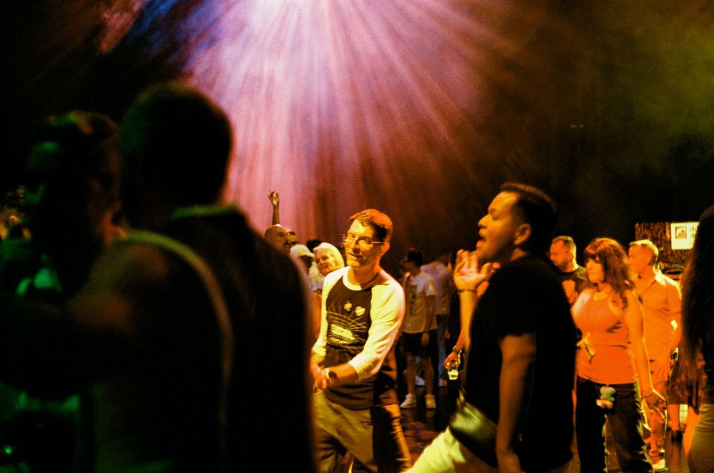 People worshipping with raised hands under dramatic pink stage lighting at a church service or concert.