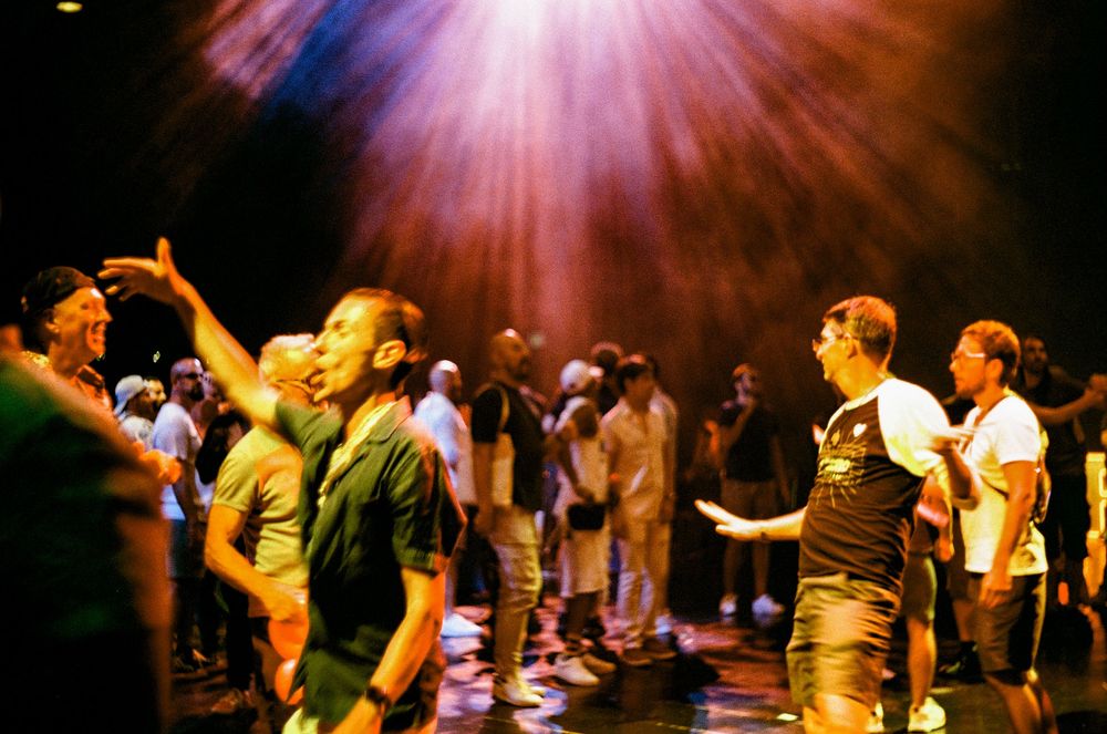 People dancing on a dark dance floor with dramatic pink lighting and crowd in the background.