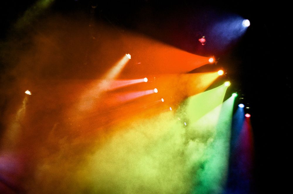 Colorful stage lights illuminate fog with vibrant red, green and blue hues creating an atmospheric effect at a performance.