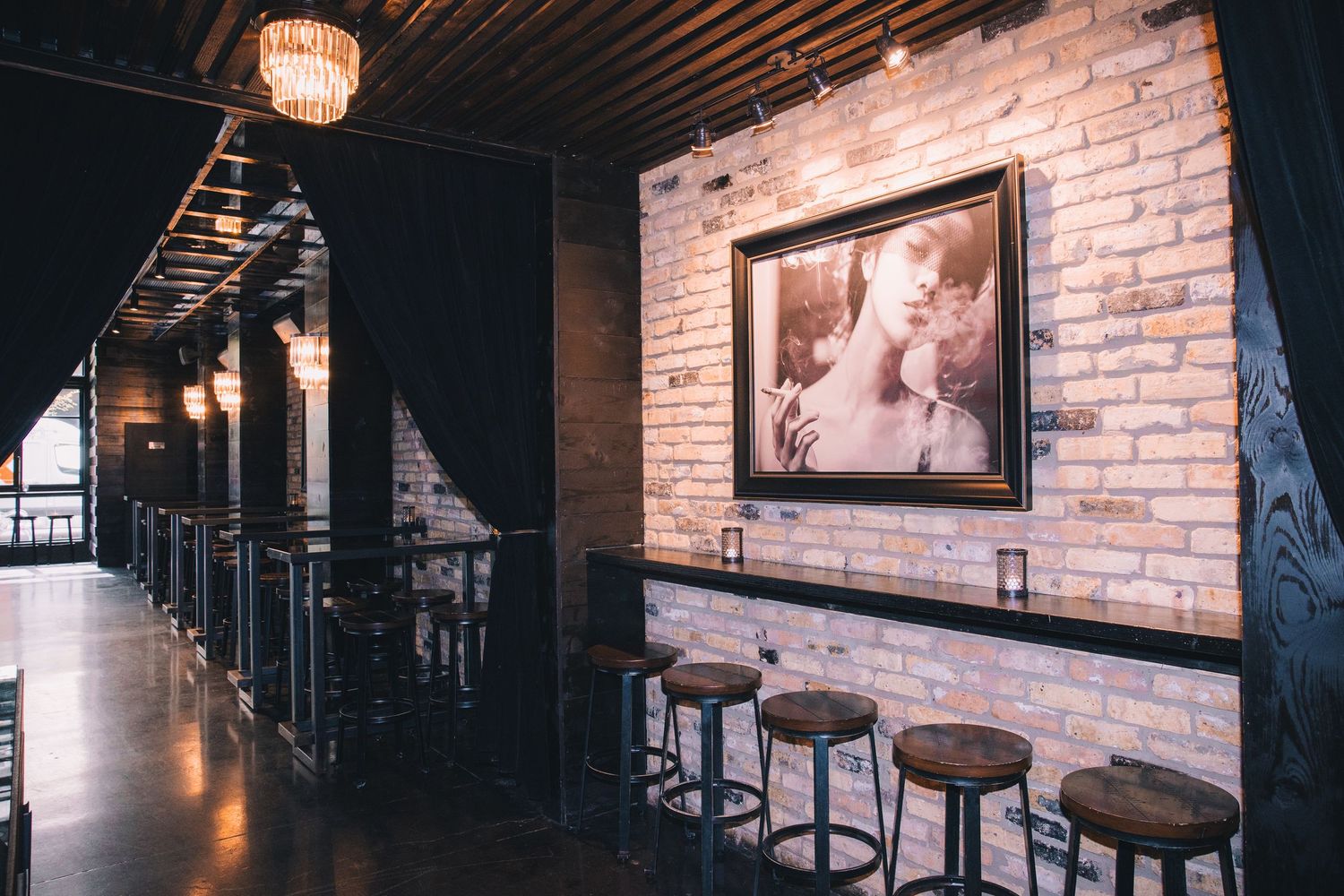 Upscale bar interior featuring brick walls, vintage photographs, and moody lighting creating an intimate atmosphere.